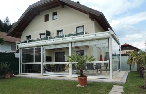 An Hausecke angrenzender Wintergarten mit Rollfenstern an den Seiten